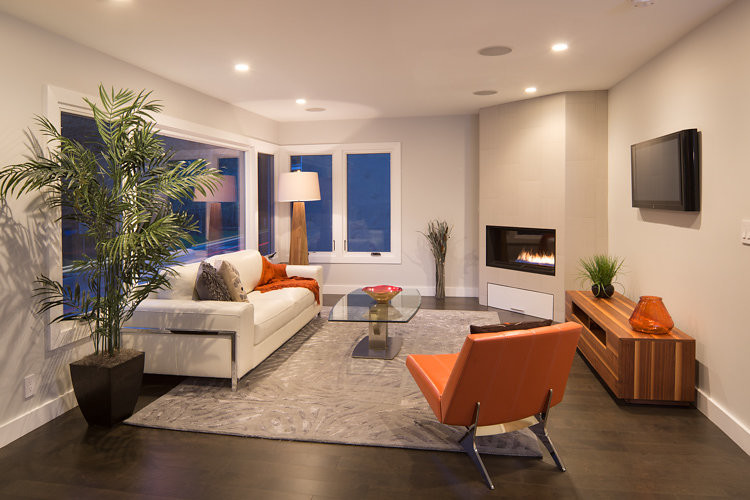 Immagine di un piccolo soggiorno minimalista aperto con pareti grigie, parquet scuro, camino ad angolo, cornice del camino piastrellata e TV a parete
