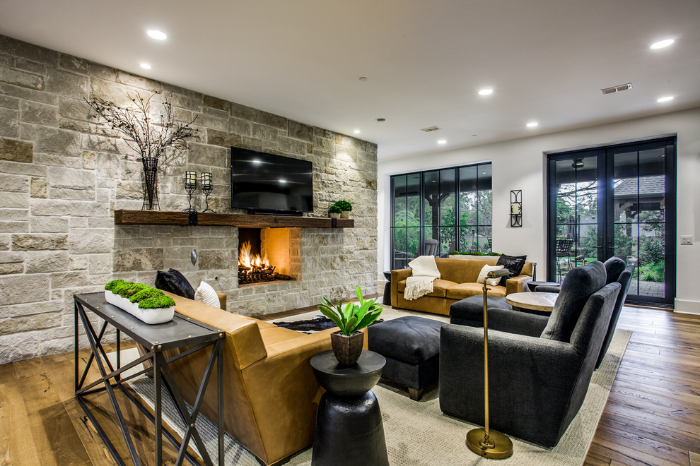 ダラスにあるトランジショナルスタイルのおしゃれなリビング (白い壁、無垢フローリング、両方向型暖炉、石材の暖炉まわり、壁掛け型テレビ、茶色い床) の写真