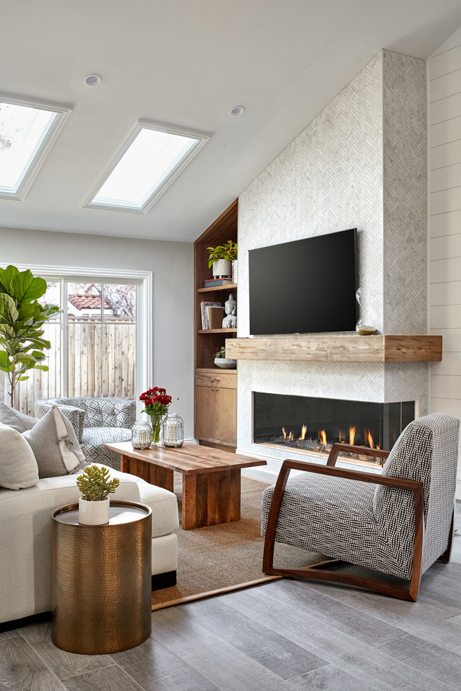 На фото: гостиная комната в морском стиле с белыми стенами, горизонтальным камином, фасадом камина из плитки, телевизором на стене и серым полом с