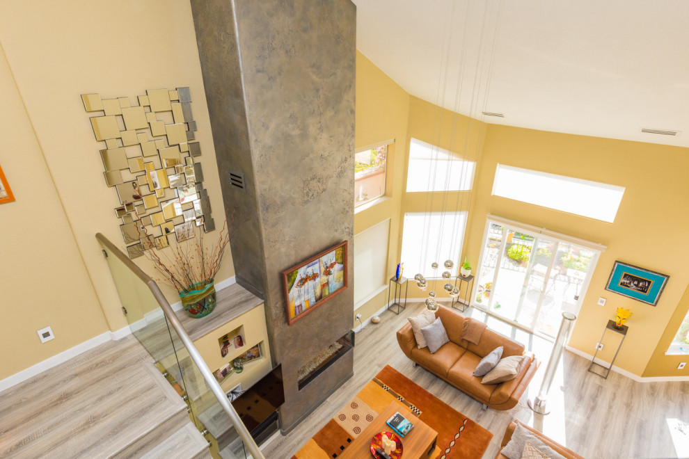 На фото: открытая гостиная комната среднего размера в стиле модернизм с желтыми стенами, полом из ламината, горизонтальным камином, фасадом камина из штукатурки и серым полом с
