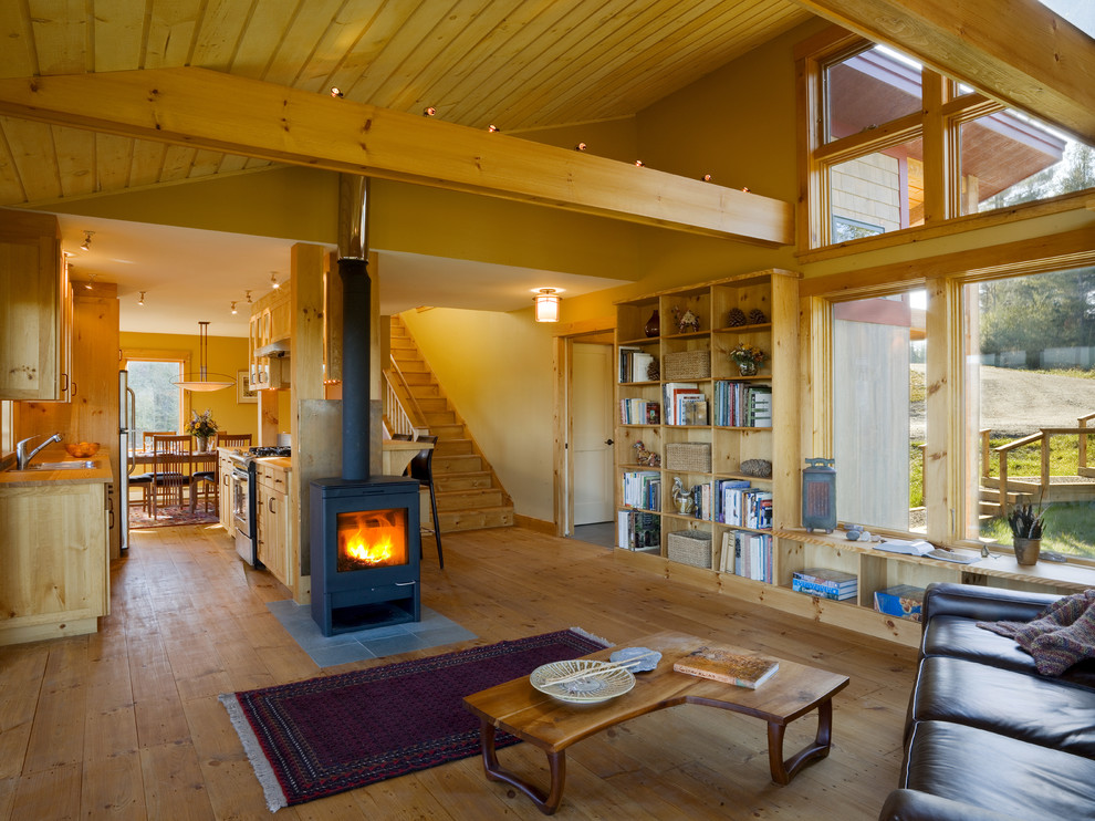 На фото: открытая гостиная комната в стиле рустика с желтыми стенами, печью-буржуйкой и ковром на полу