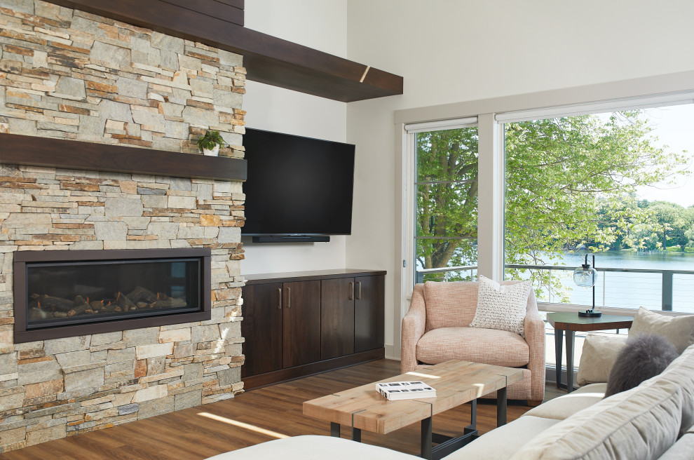 Offenes Modernes Wohnzimmer mit weißer Wandfarbe, braunem Holzboden, Gaskamin, Kaminumrandung aus Stein, TV-Wand und braunem Boden in Grand Rapids