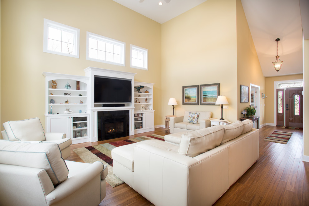 Cette image montre un salon traditionnel de taille moyenne et ouvert avec un mur jaune, un sol en bois brun, une cheminée standard, un manteau de cheminée en bois, un téléviseur encastré, un sol marron et éclairage.