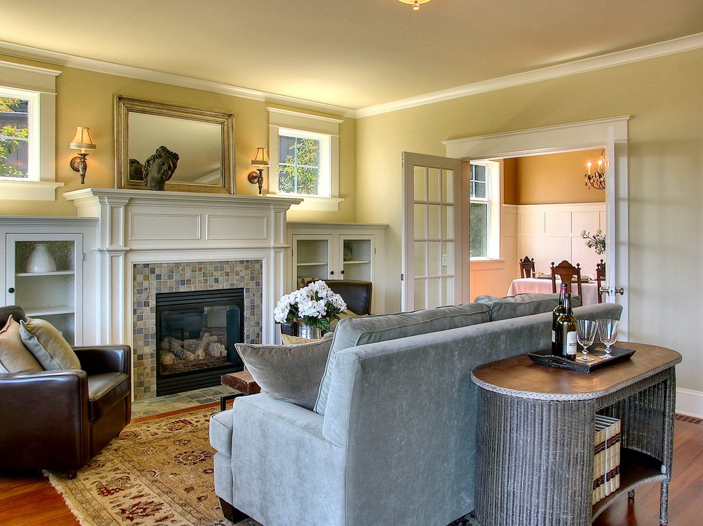 Идея дизайна: гостиная комната среднего размера в классическом стиле с фасадом камина из плитки, желтыми стенами, паркетным полом среднего тона, стандартным камином и ковром на полу