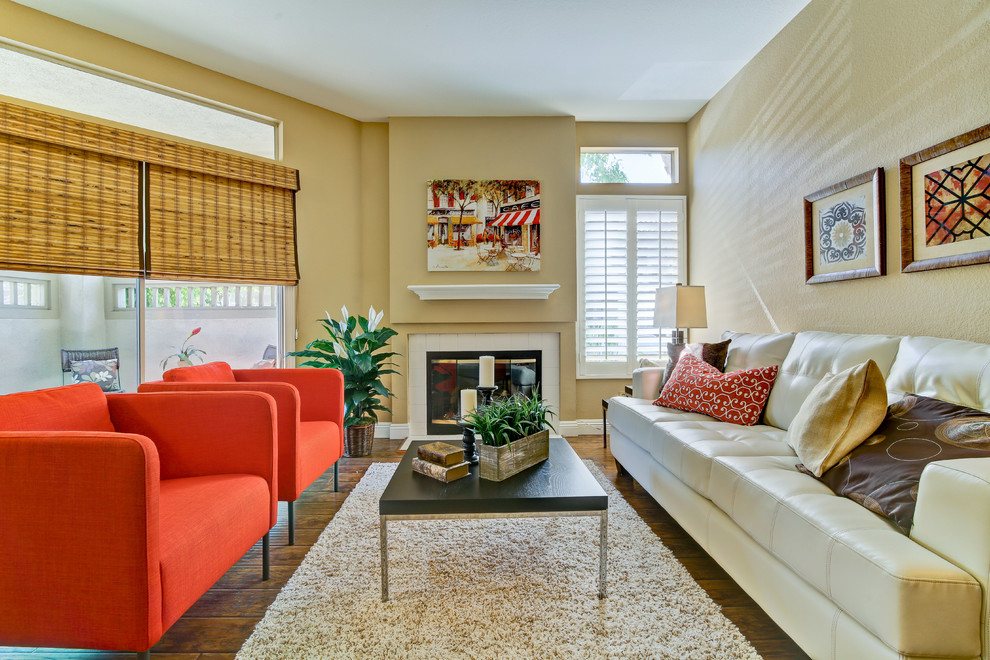 Offenes Wohnzimmer mit beiger Wandfarbe, dunklem Holzboden, Kamin und gefliester Kaminumrandung in Orange County