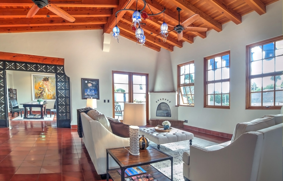 Mediterranes Wohnzimmer mit beiger Wandfarbe, Keramikboden, Eckkamin, verputzter Kaminumrandung und rotem Boden in Santa Barbara