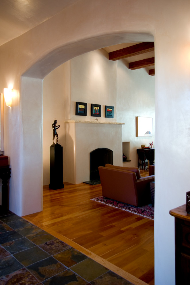 アルバカーキにある高級な広いサンタフェスタイルのおしゃれなリビング (白い壁、無垢フローリング、標準型暖炉、漆喰の暖炉まわり、テレビなし) の写真