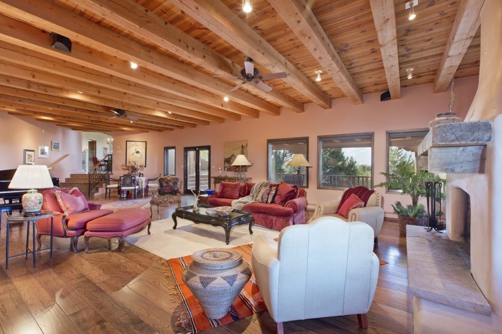 Cette image montre un salon sud-ouest américain de taille moyenne et ouvert avec un mur beige, un sol en bois brun, une cheminée standard, un manteau de cheminée en béton, aucun téléviseur et un sol marron.