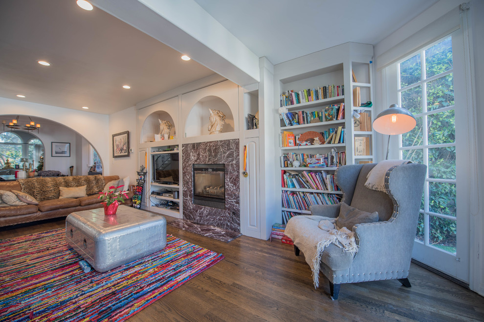 Cette image montre un salon bohème ouvert avec une bibliothèque ou un coin lecture, un mur blanc, parquet foncé, une cheminée standard, un téléviseur indépendant et un sol marron.