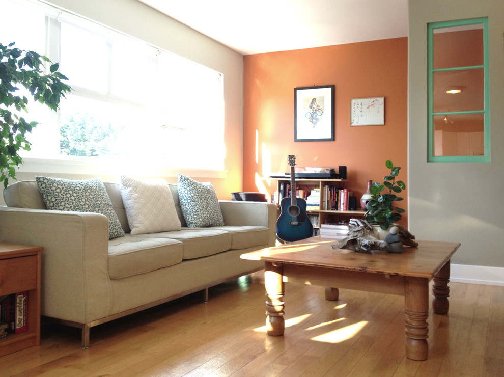 Esempio di un soggiorno minimal di medie dimensioni e aperto con sala formale, pareti arancioni, parquet chiaro e TV a parete