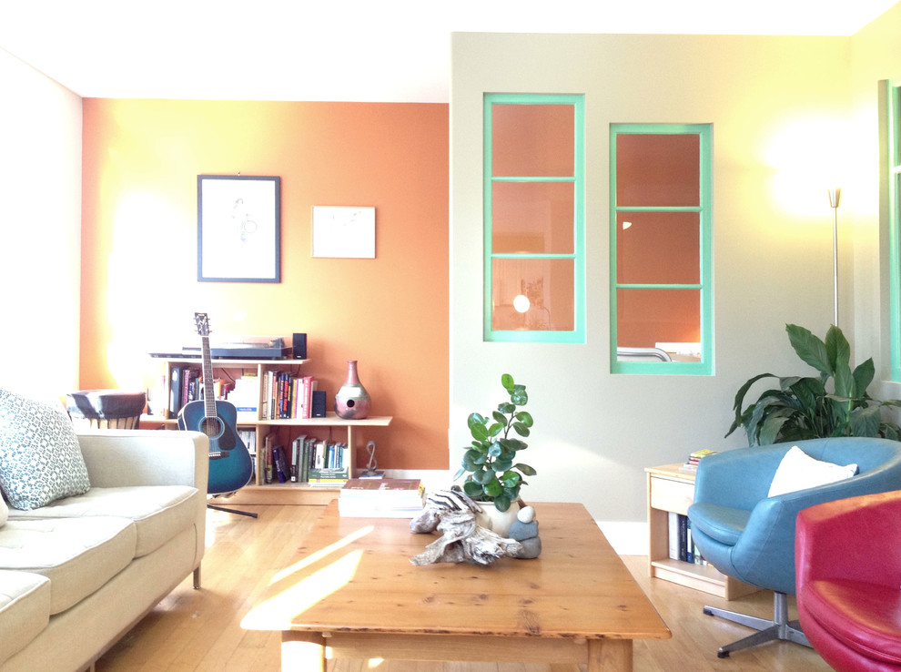 Ejemplo de salón para visitas abierto contemporáneo de tamaño medio con parades naranjas, suelo de madera clara y televisor colgado en la pared