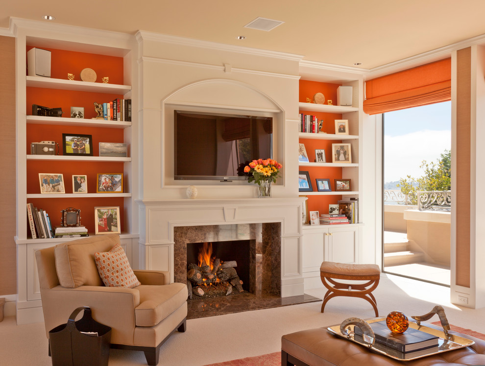 サンフランシスコにある高級な中くらいなトラディショナルスタイルのおしゃれなリビング (オレンジの壁、標準型暖炉、石材の暖炉まわり、壁掛け型テレビ、ベージュの床、カーペット敷き) の写真