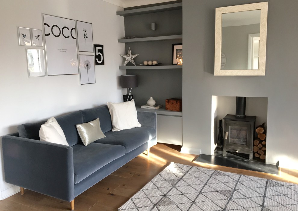 Mittelgroßes, Offenes Skandinavisches Wohnzimmer mit grauer Wandfarbe, braunem Holzboden, Kaminofen und verputzter Kaminumrandung in Surrey