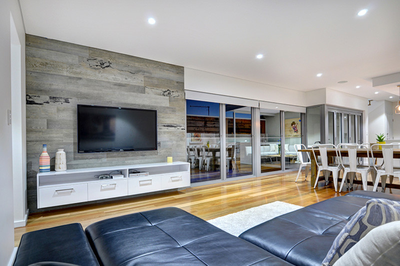 Imagen de salón abierto actual de tamaño medio con televisor colgado en la pared, paredes blancas y suelo de madera en tonos medios