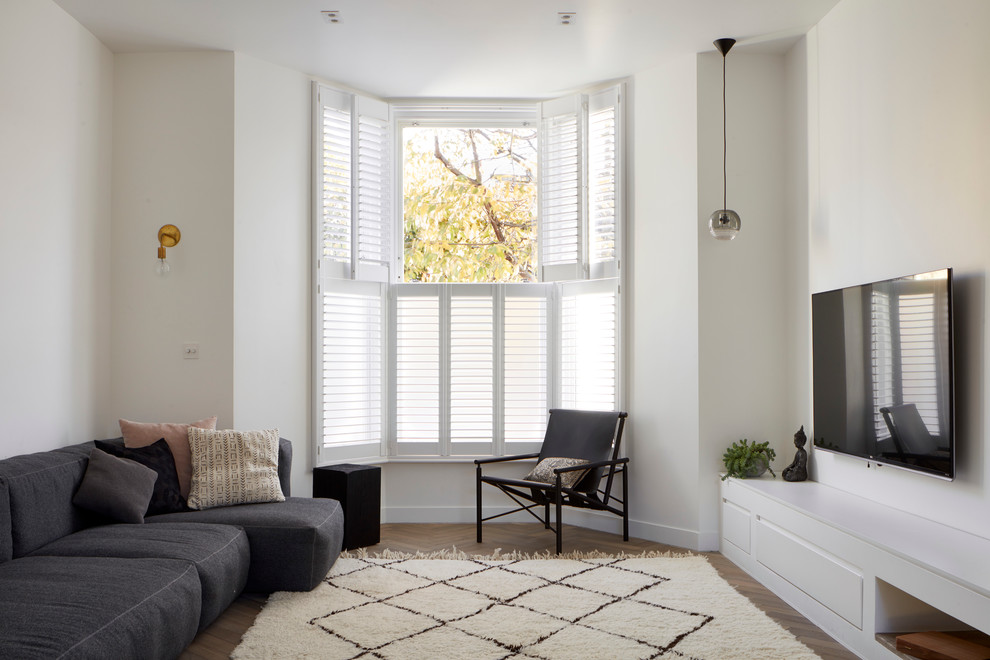 Esempio di un grande soggiorno design aperto con pareti bianche, pavimento in legno massello medio, TV a parete e pavimento marrone