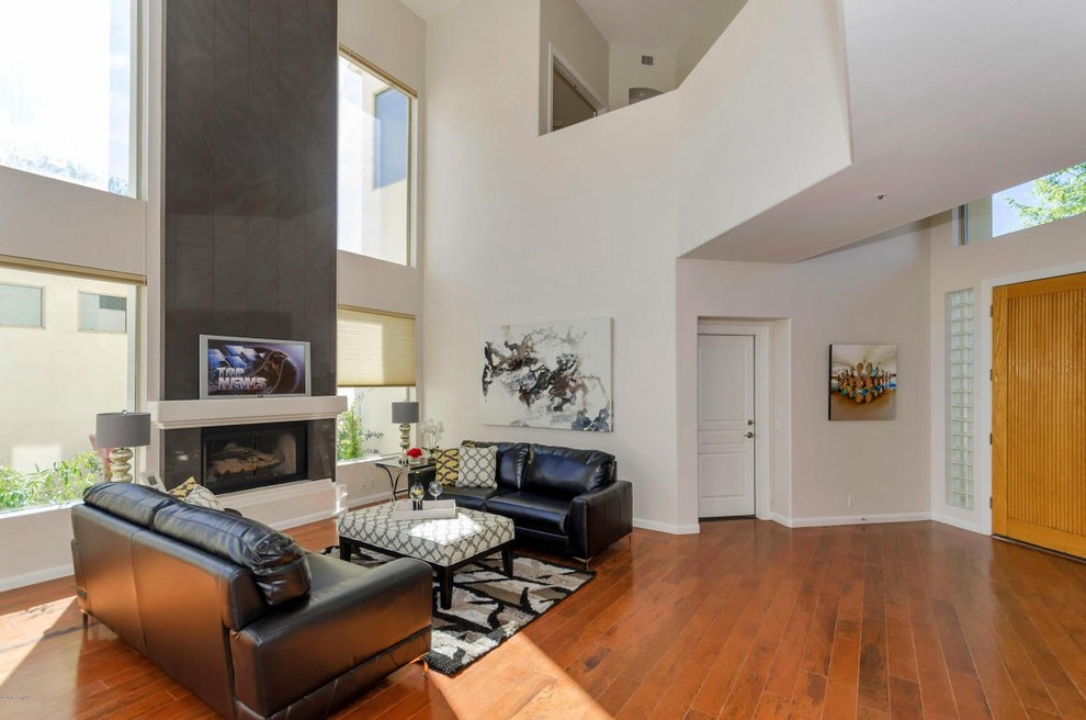 Mittelgroßes, Offenes Modernes Wohnzimmer mit grauer Wandfarbe, braunem Holzboden, Kamin, gefliester Kaminumrandung und TV-Wand in Phoenix