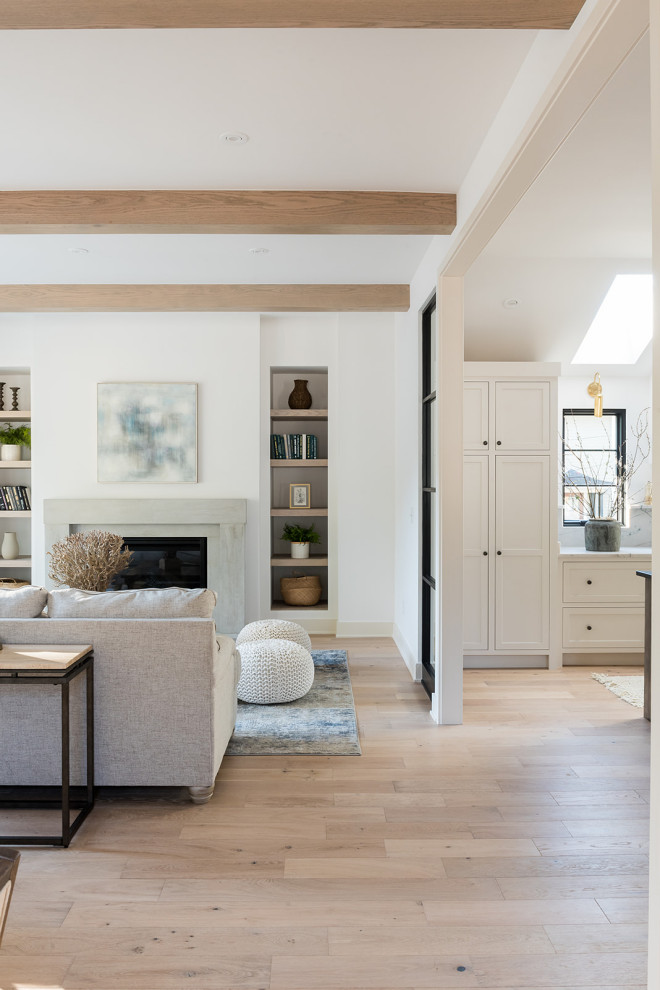 Aménagement d'un salon moderne avec un mur blanc, parquet clair, une cheminée standard, un manteau de cheminée en pierre, un sol marron et poutres apparentes.