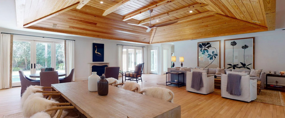 Aménagement d'un grand salon bord de mer ouvert avec un mur blanc, parquet clair, une cheminée standard, un manteau de cheminée en pierre, un téléviseur encastré, un sol marron et un plafond en bois.