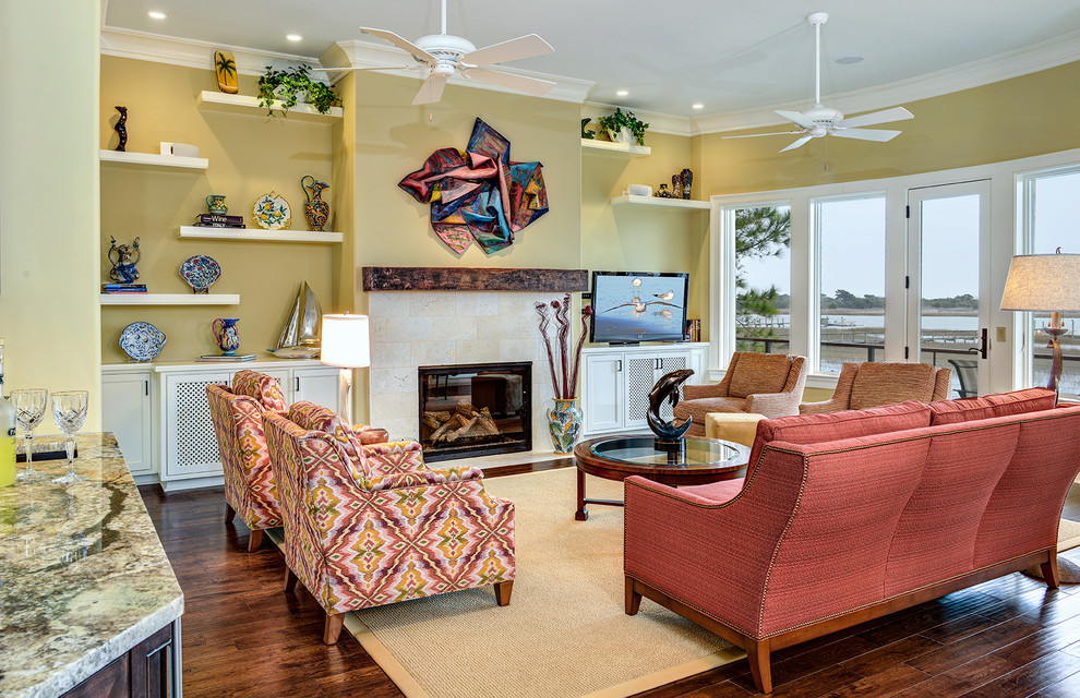 Пример оригинального дизайна: открытая гостиная комната в морском стиле с желтыми стенами, темным паркетным полом, стандартным камином, фасадом камина из плитки и отдельно стоящим телевизором