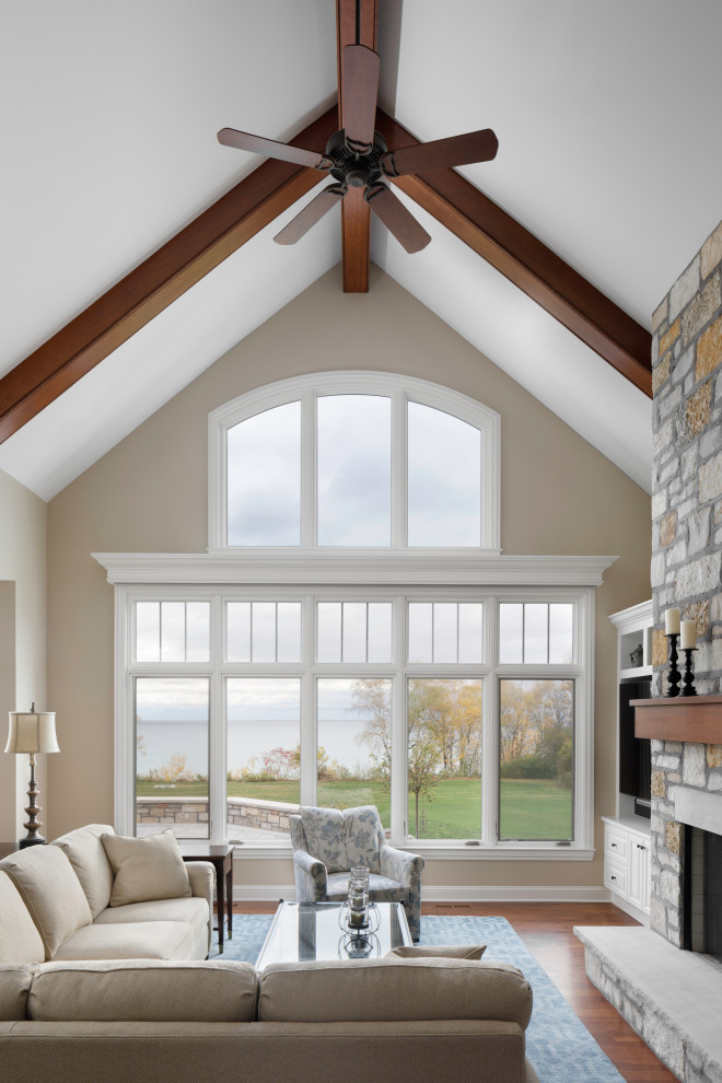 Inspiration for a large traditional mezzanine living room in Milwaukee with beige walls, dark hardwood flooring, a standard fireplace, a stone fireplace surround, brown floors and a vaulted ceiling.