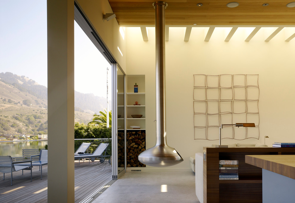 Идея дизайна: открытая гостиная комната среднего размера в морском стиле с бежевыми стенами, бетонным полом, подвесным камином и фасадом камина из металла