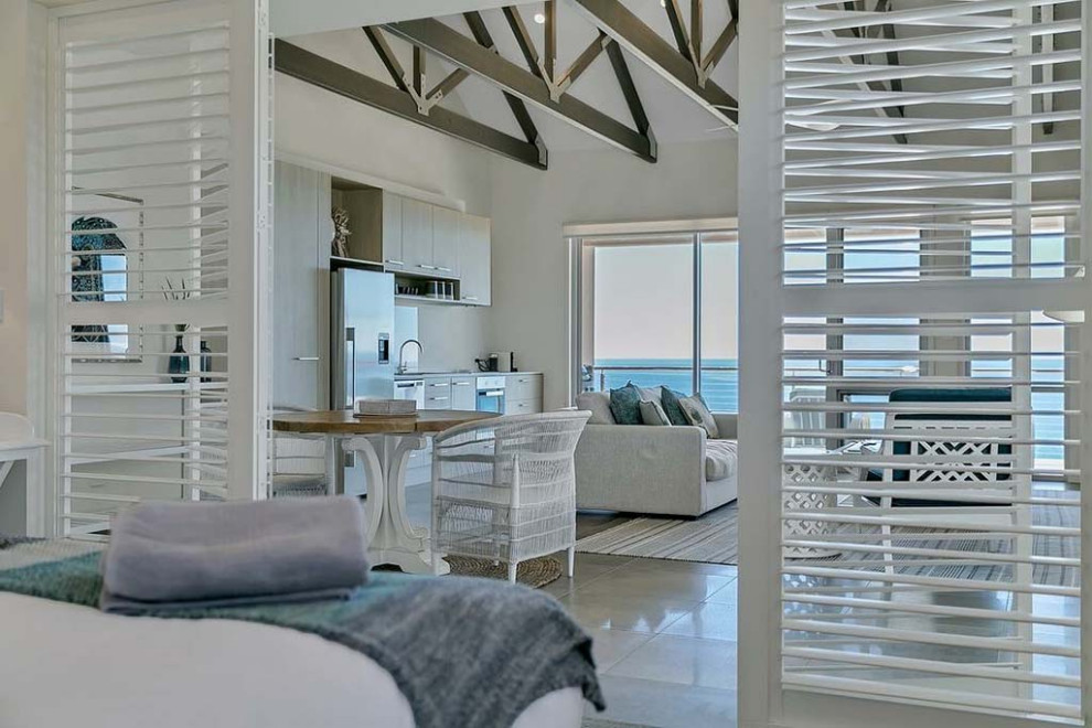 Идея дизайна: большая открытая гостиная комната в морском стиле с белыми стенами, полом из керамогранита, фасадом камина из камня, телевизором на стене и серым полом