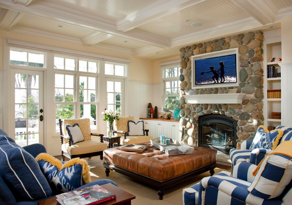 На фото: гостиная комната в классическом стиле с бежевыми стенами, стандартным камином, фасадом камина из камня, телевизором на стене и синим диваном