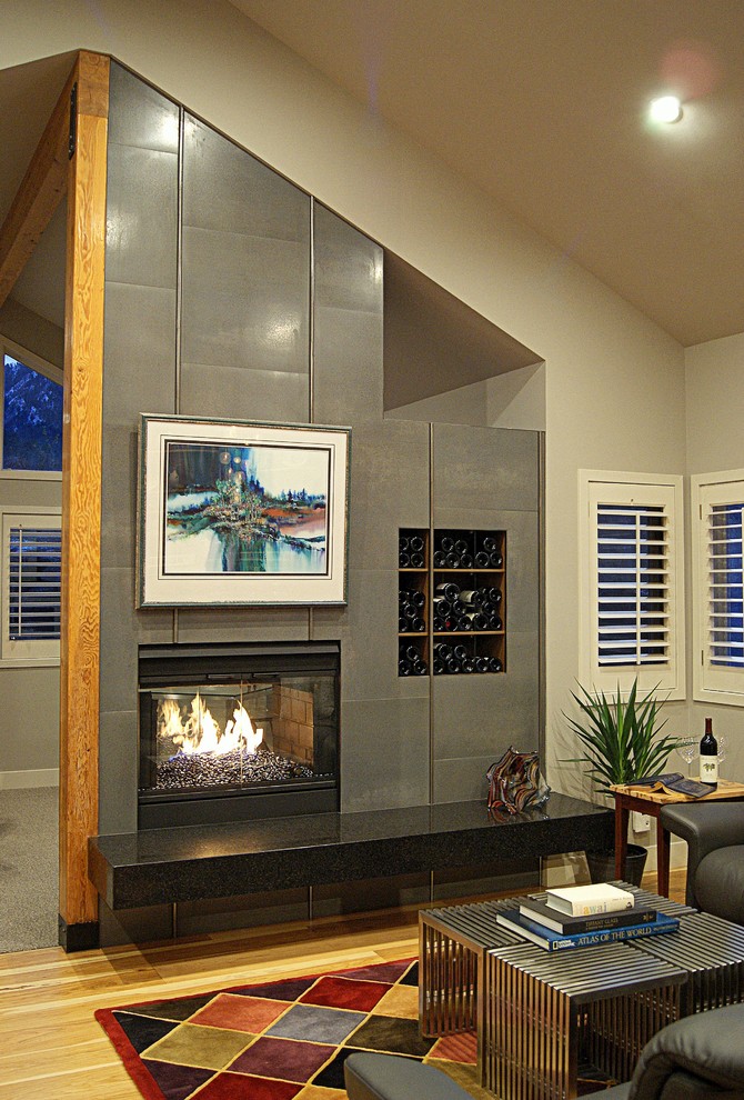 Cette image montre un grand salon design avec un mur gris, un sol en bois brun, une cheminée double-face et un manteau de cheminée en carrelage.