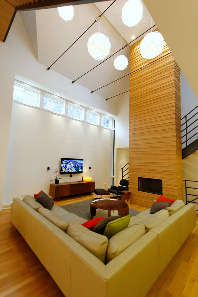 Modelo de salón abierto moderno de tamaño medio con paredes blancas, suelo de madera clara, todas las chimeneas, marco de chimenea de madera y televisor colgado en la pared