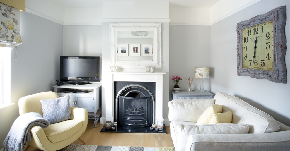 Example of a small trendy formal and enclosed light wood floor living room design in Surrey with gray walls, a standard fireplace, a wood fireplace surround and a tv stand