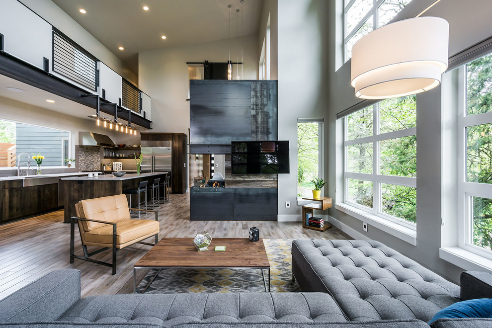 Foto de salón abierto moderno grande con paredes grises, suelo de madera en tonos medios, chimenea de doble cara y televisor colgado en la pared