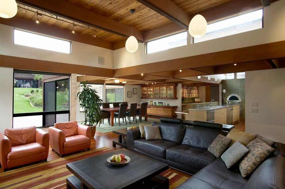 На фото: большая открытая гостиная комната в современном стиле с паркетным полом среднего тона, коричневыми стенами, стандартным камином, фасадом камина из плитки, телевизором на стене и коричневым полом