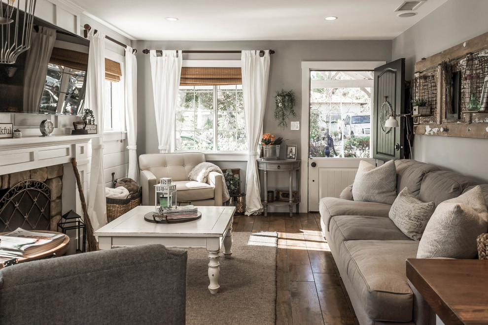 Cottage chic medium tone wood floor and brown floor living room photo in Orange County with gray walls, a standard fireplace, a stone fireplace and a wall-mounted tv