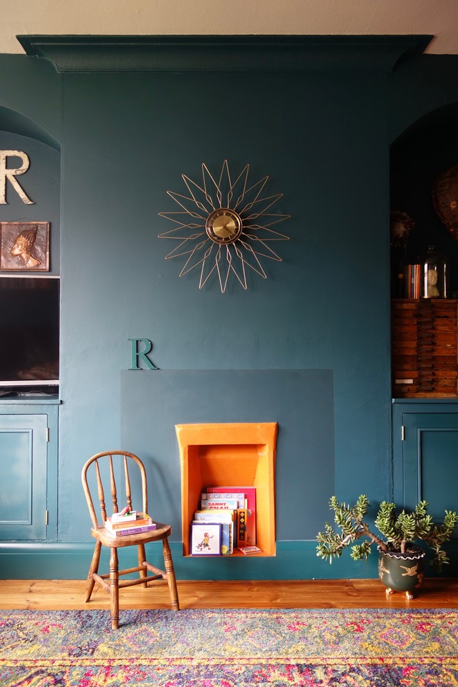 Großes, Offenes Stilmix Wohnzimmer ohne Kamin mit braunem Holzboden, verputzter Kaminumrandung, freistehendem TV und blauer Wandfarbe in Sonstige