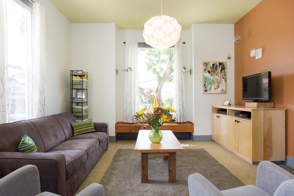 Foto på ett funkis vardagsrum, med ett finrum, orange väggar, heltäckningsmatta och en fristående TV