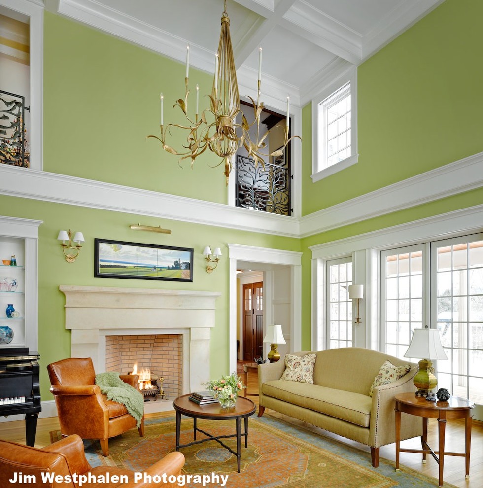 Стильный дизайн: большая парадная, двухуровневая гостиная комната в классическом стиле с зелеными стенами, паркетным полом среднего тона, стандартным камином и фасадом камина из камня - последний тренд