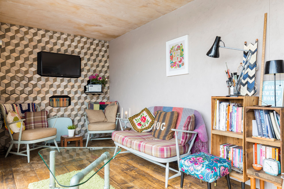 Cette image montre un petit salon bohème avec une bibliothèque ou un coin lecture, un sol en bois brun et un téléviseur fixé au mur.