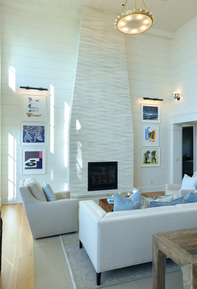 На фото: огромная открытая гостиная комната в классическом стиле с белыми стенами, светлым паркетным полом, стандартным камином и фасадом камина из камня