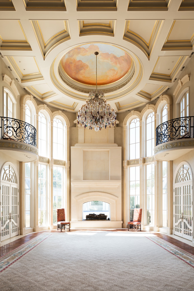 Пример оригинального дизайна: огромная парадная, открытая гостиная комната в классическом стиле с бежевыми стенами, темным паркетным полом, двусторонним камином и фасадом камина из камня