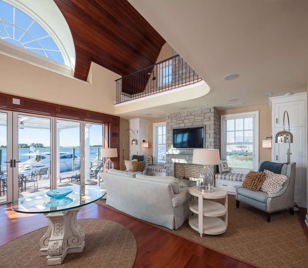 This is an example of a beach style mezzanine living room in New York with beige walls, medium hardwood flooring, a two-sided fireplace, a stone fireplace surround and a wall mounted tv.