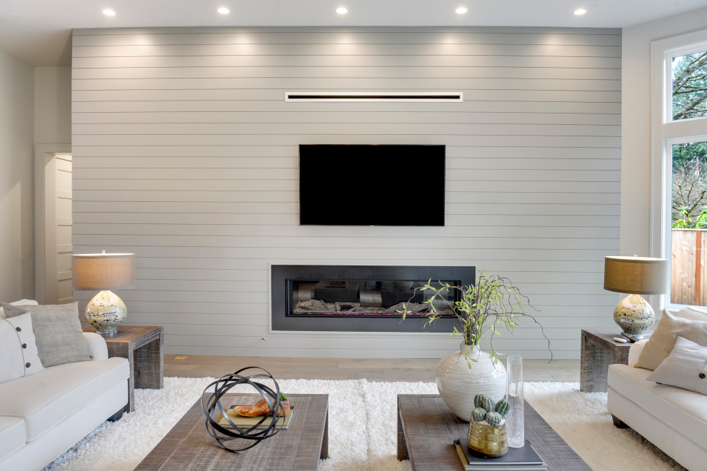 Imagen de salón abierto minimalista grande con paredes grises, suelo de madera en tonos medios, chimenea lineal, marco de chimenea de metal, televisor colgado en la pared y suelo gris