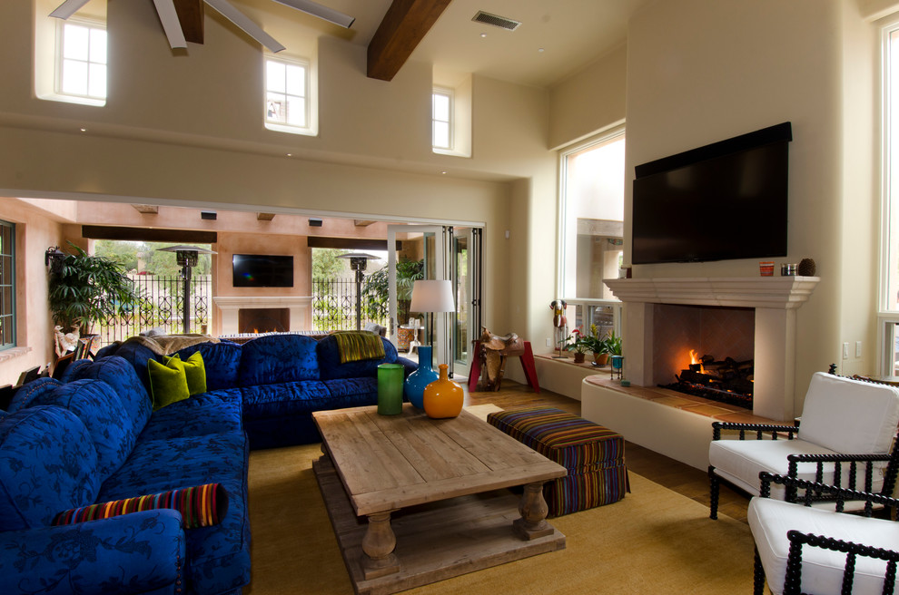 Mittelgroßes, Offenes Mediterranes Wohnzimmer mit beiger Wandfarbe, braunem Holzboden, Kamin, verputzter Kaminumrandung, TV-Wand und braunem Boden in Phoenix
