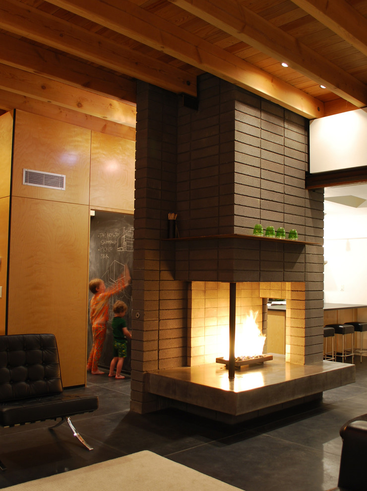 Ejemplo de salón abierto moderno pequeño con paredes grises, suelo de cemento, chimenea de doble cara, marco de chimenea de hormigón y televisor colgado en la pared