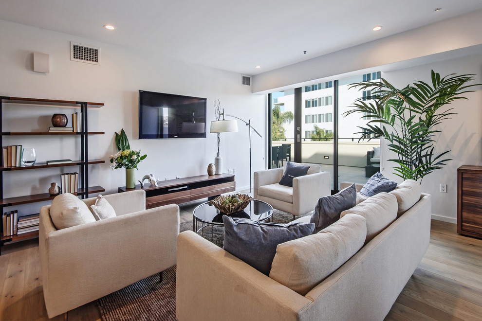Источник вдохновения для домашнего уюта: большая открытая гостиная комната в современном стиле с белыми стенами, светлым паркетным полом, телевизором на стене и коричневым полом