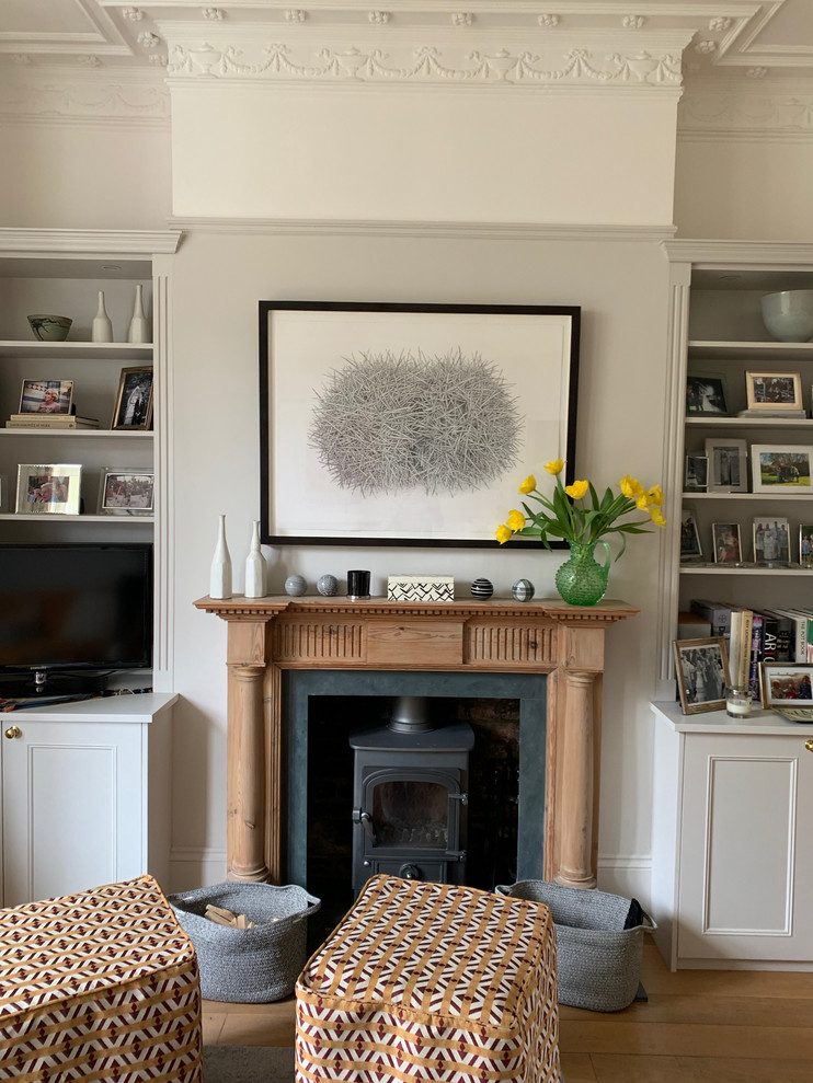 ロンドンにある高級な広いトラディショナルスタイルのおしゃれなリビング (グレーの壁、無垢フローリング、薪ストーブ、木材の暖炉まわり、据え置き型テレビ、茶色い床) の写真