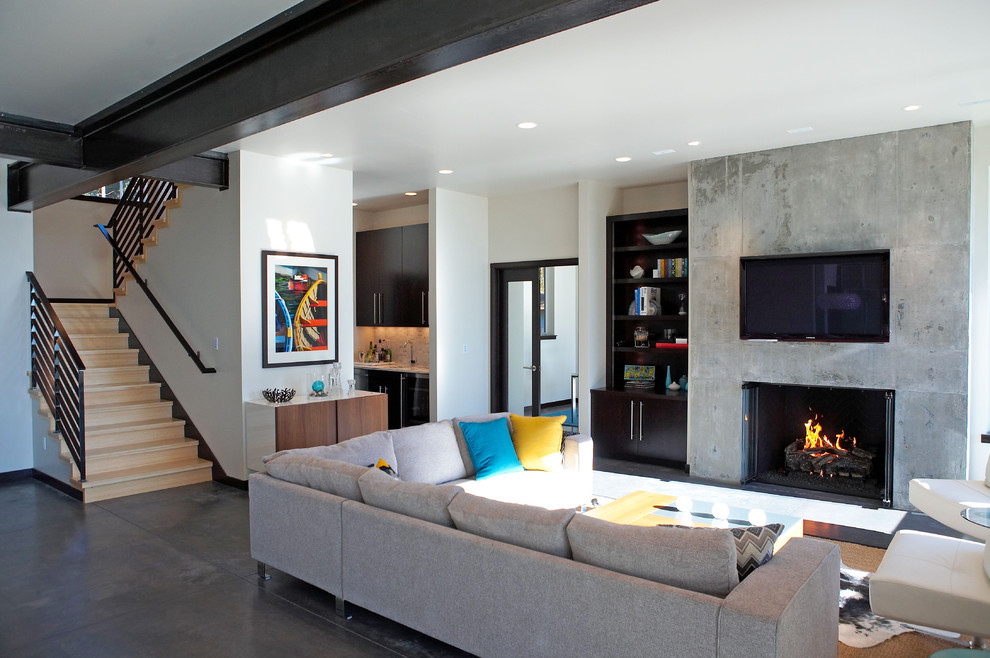 Cette image montre un salon minimaliste de taille moyenne et ouvert avec un bar de salon, une cheminée standard, un manteau de cheminée en béton, un téléviseur fixé au mur et un sol gris.