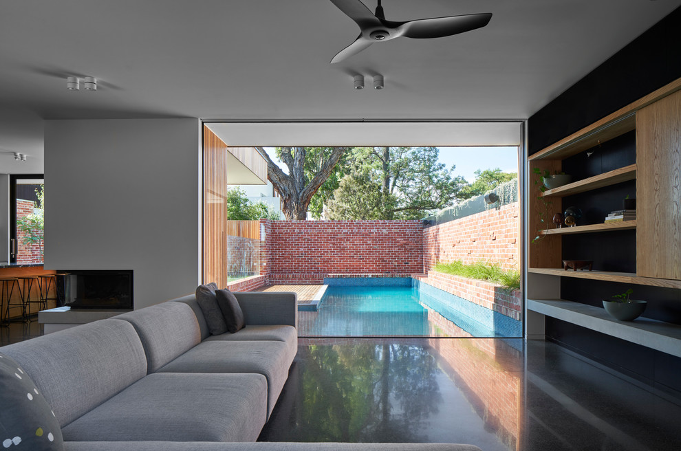 На фото: гостиная комната в современном стиле с бетонным полом, угловым камином, фасадом камина из бетона, скрытым телевизором и серым полом