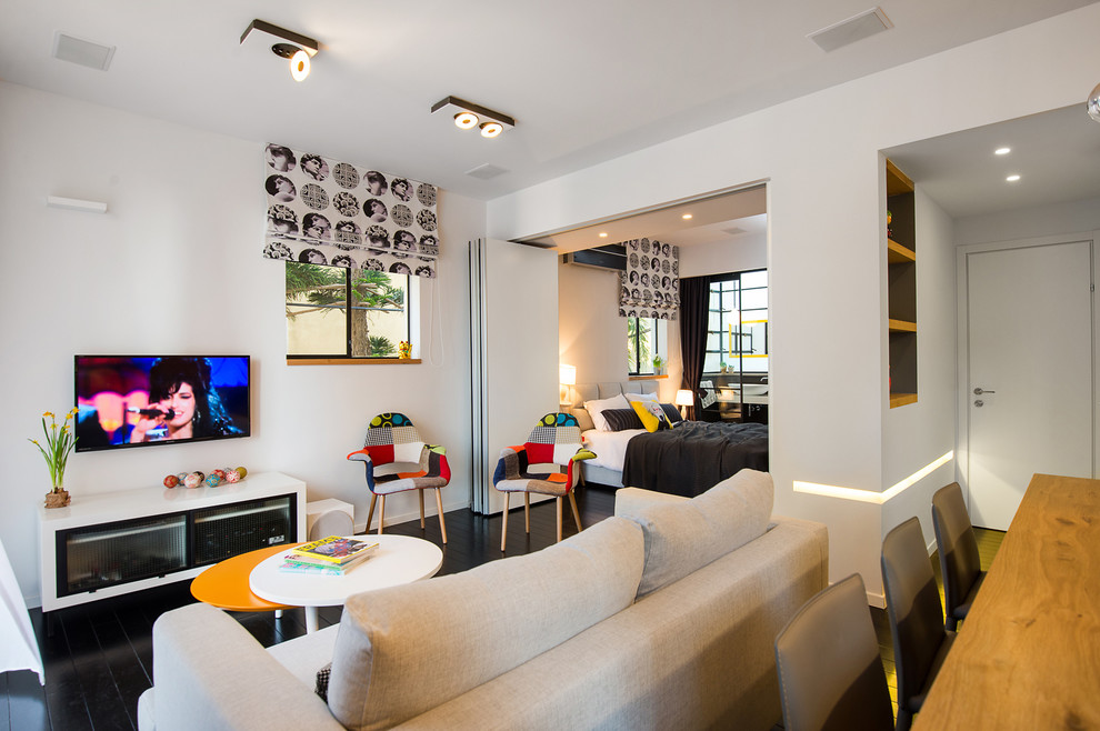 Kleines Modernes Wohnzimmer mit weißer Wandfarbe, gebeiztem Holzboden und TV-Wand in Tel Aviv