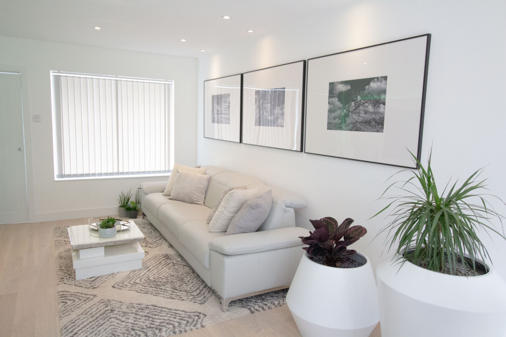 Modelo de salón para visitas abierto moderno pequeño sin chimenea con paredes blancas, suelo de madera clara, televisor retractable y suelo beige