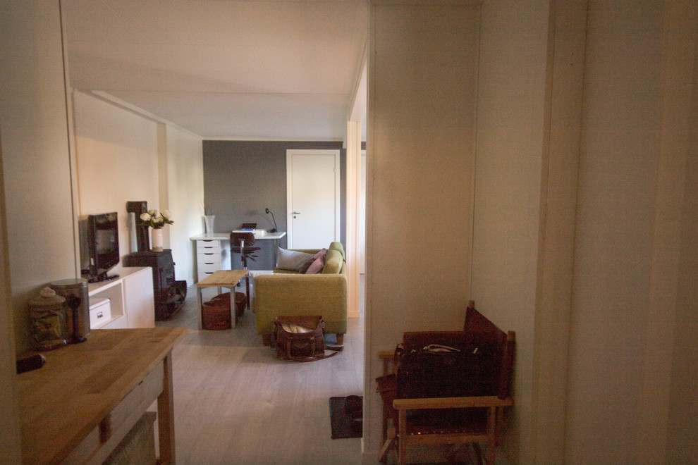 Ejemplo de salón abierto escandinavo pequeño con paredes blancas, suelo laminado, estufa de leña, marco de chimenea de metal, televisor independiente y suelo gris
